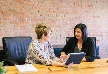 Two people sitting at a wooden table looking at a tablet, discussing what it takes for effective sales leadership.